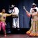 2 performers dance on stage while a band plays behind them